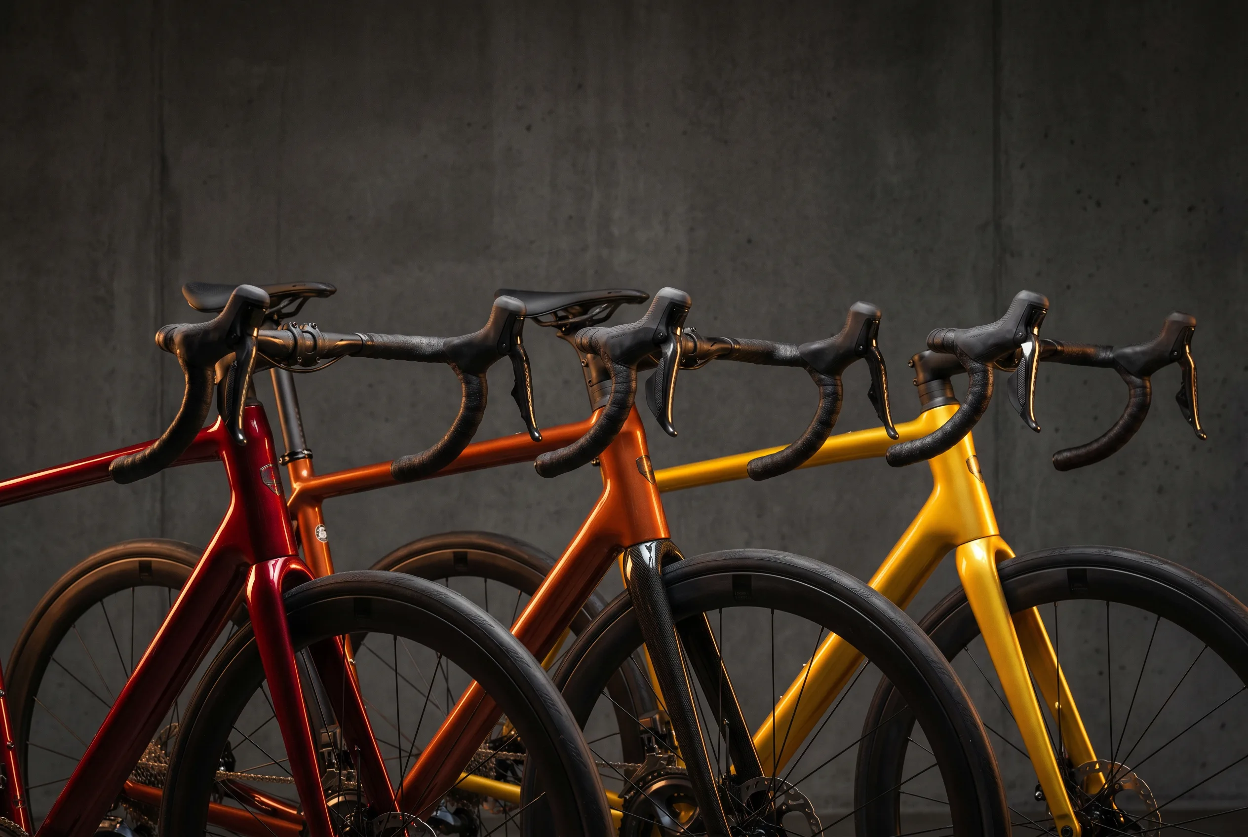 Three road bicycles in red, orange, and yellow parked against a concrete wall